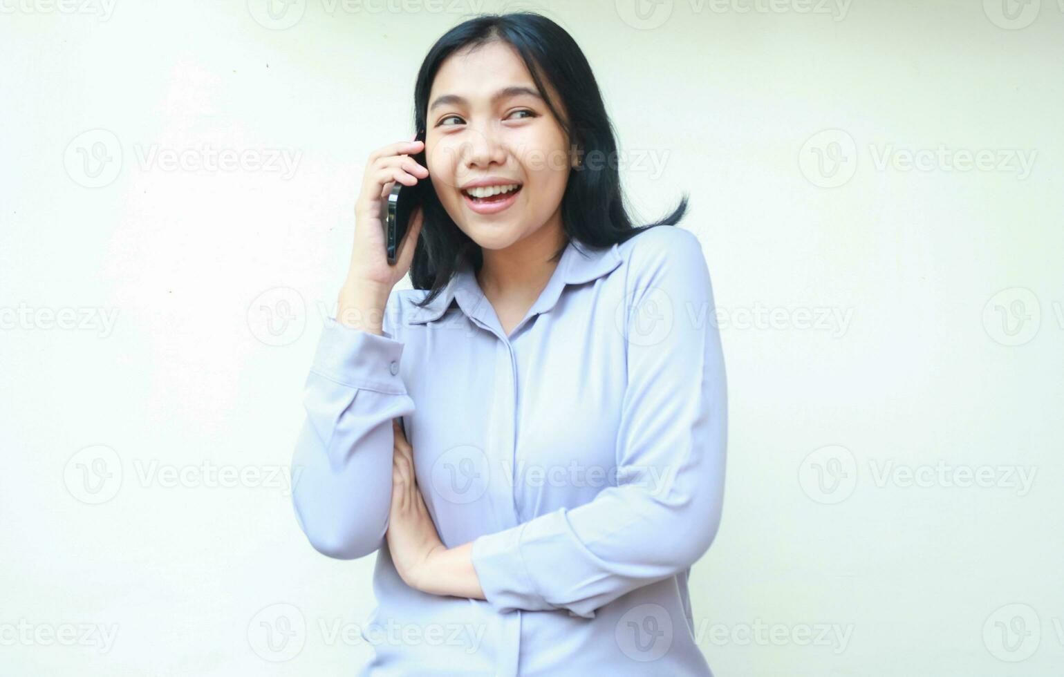 hermosa asiático joven negocio mujer emocionado teniendo conversacion Hablando en móvil teléfono con doblada brazo y Mira lejos, vestir formal traje aislado terminado blanco antecedentes foto