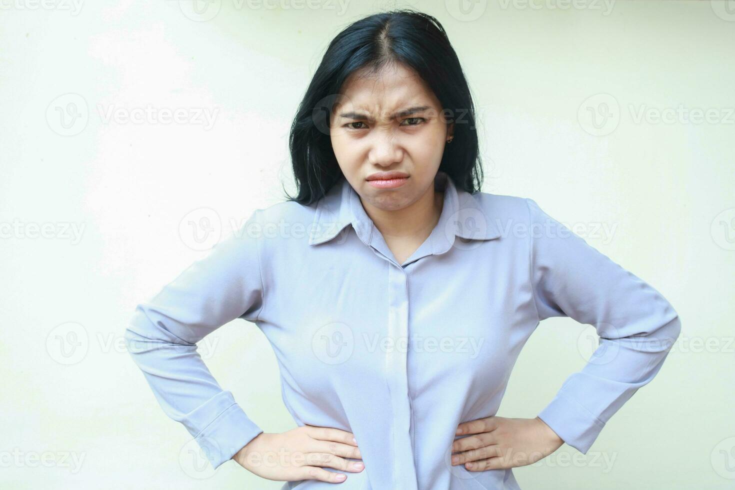 portrait of upset dissappointed asian young business woman looking to camera with angry face expression and hand on waist wearing formal suit isolated over white background photo