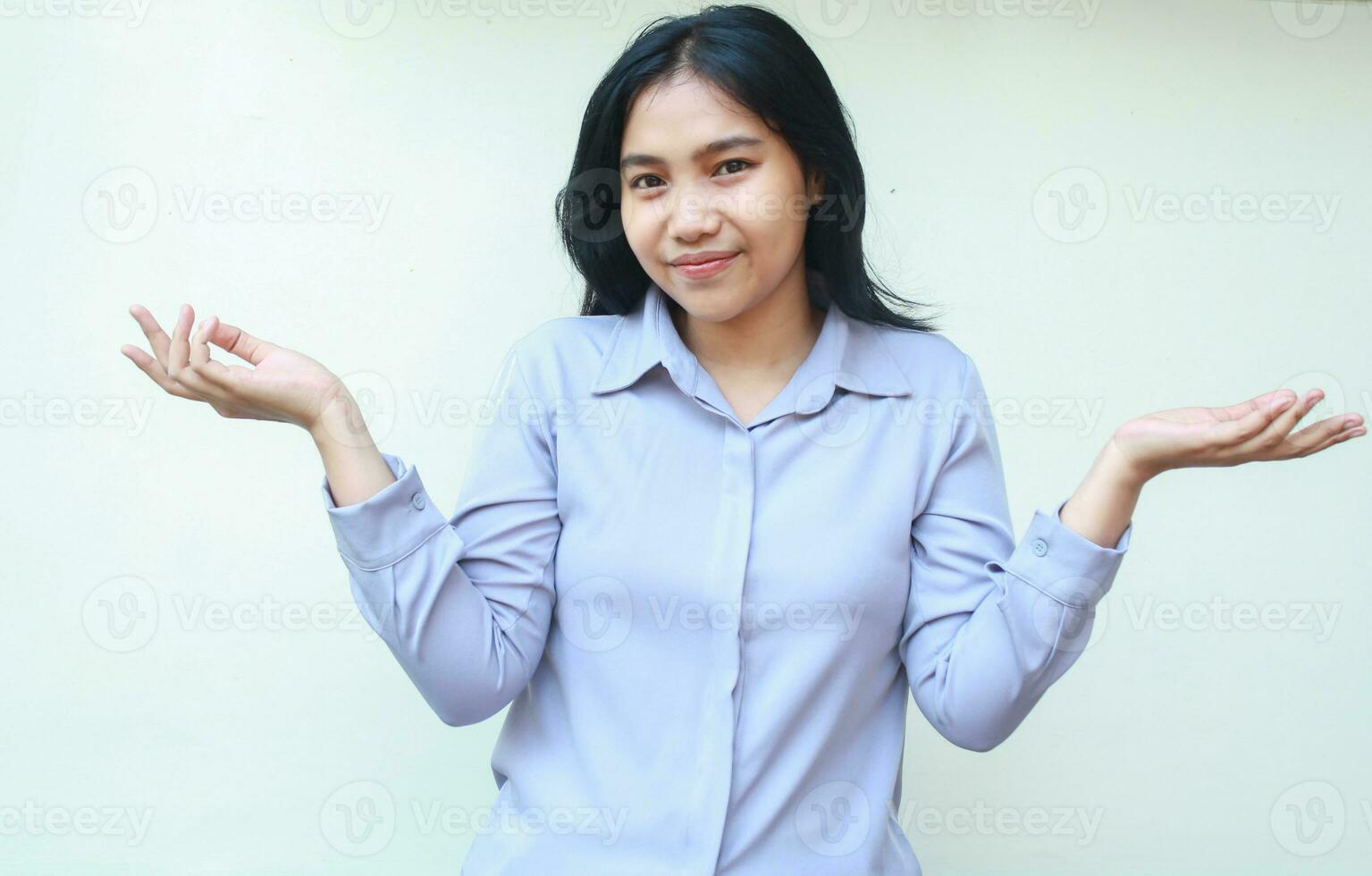 peaceful asian woman looking to camera with happy face do presenting gesture with palm sideways, considering imaginary product, wear formal shirt, isolated in white background photo