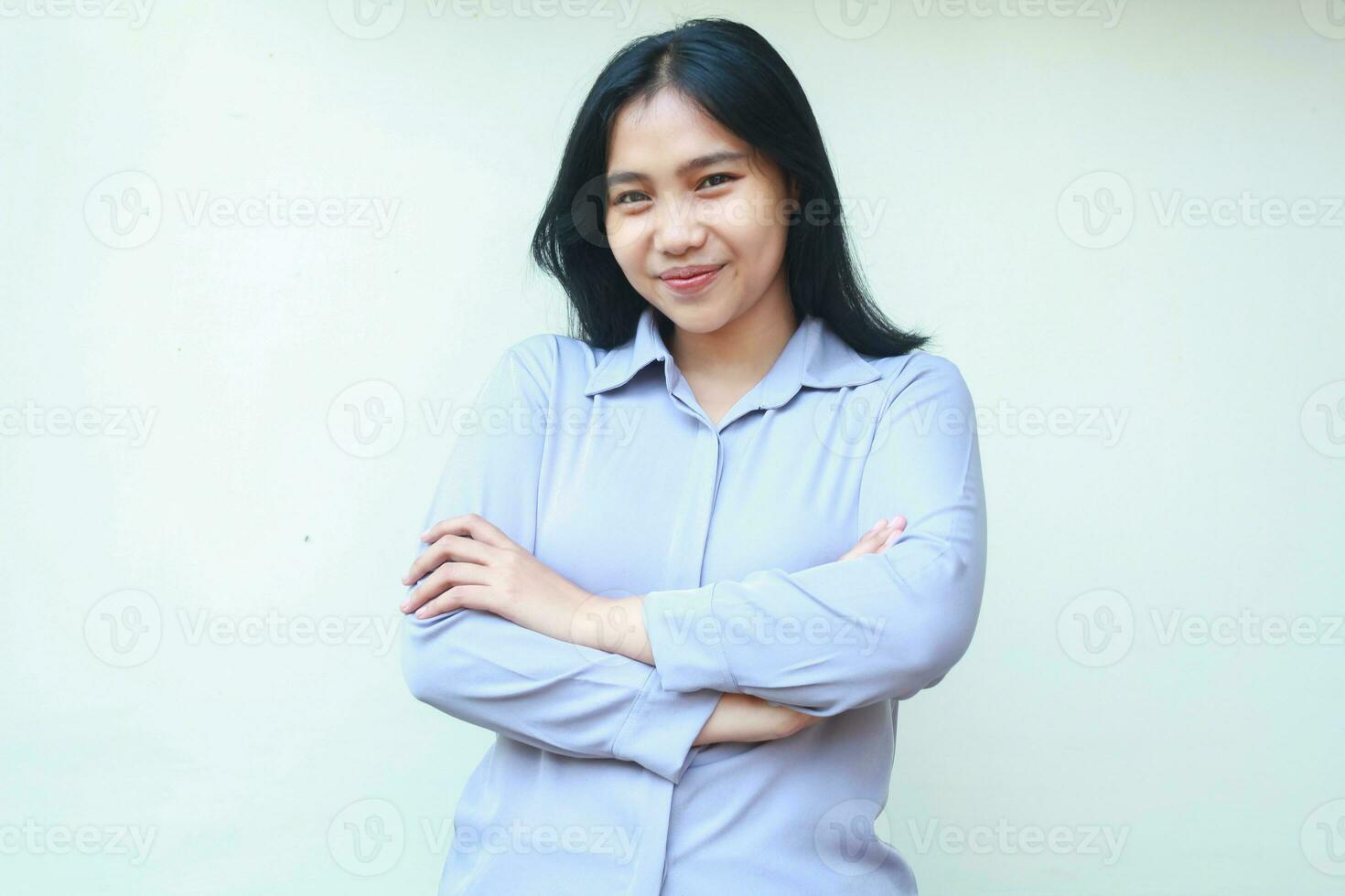 pretty asian young woman look to camera with happy face and folded arm wear formal shirt standing over white background photo