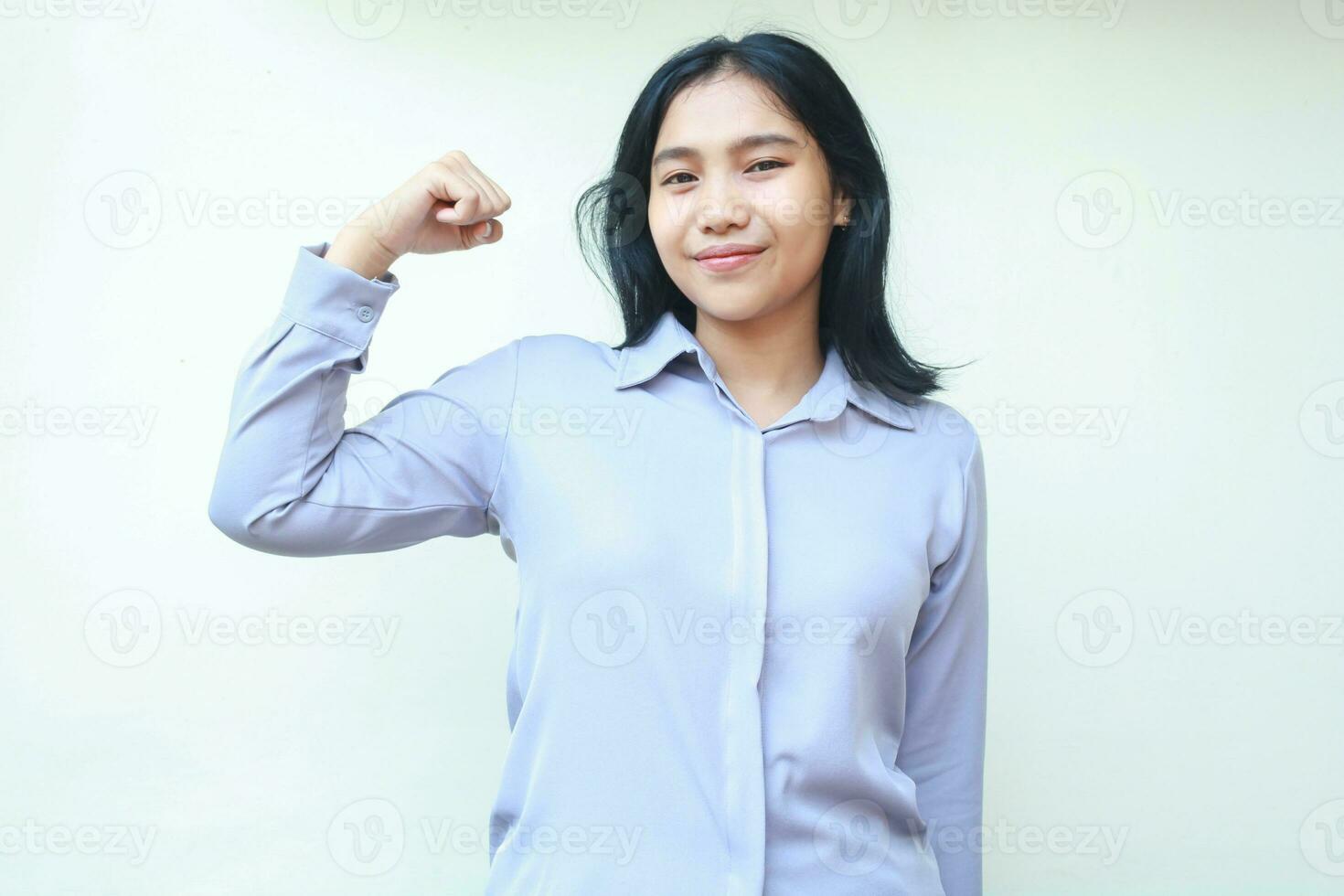 peaceful young asian business woman show strength bicep muscle with raising arm fist looking at camera with smiling relax expression, wear formal shirt, isolated on white background photo