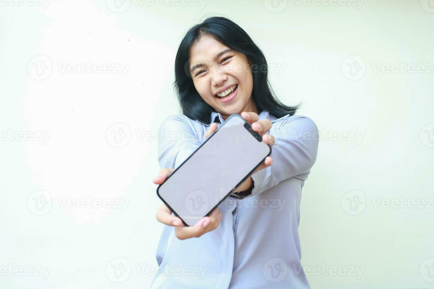 playful asian young business woman excited showing mobile phone white screen to camera with smiling satisfaction expression, app promotion mock up, dressed in formal shirt isolated on white background photo