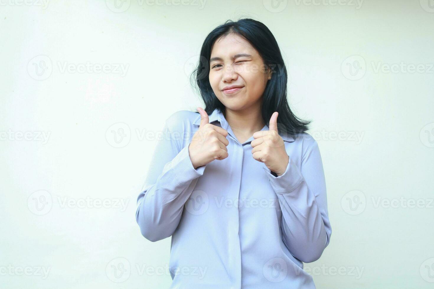 satisfied pretty asian young business woman giving two thumbs up felling happy look at camera with blink eye wear formal shirt isolated on white background photo