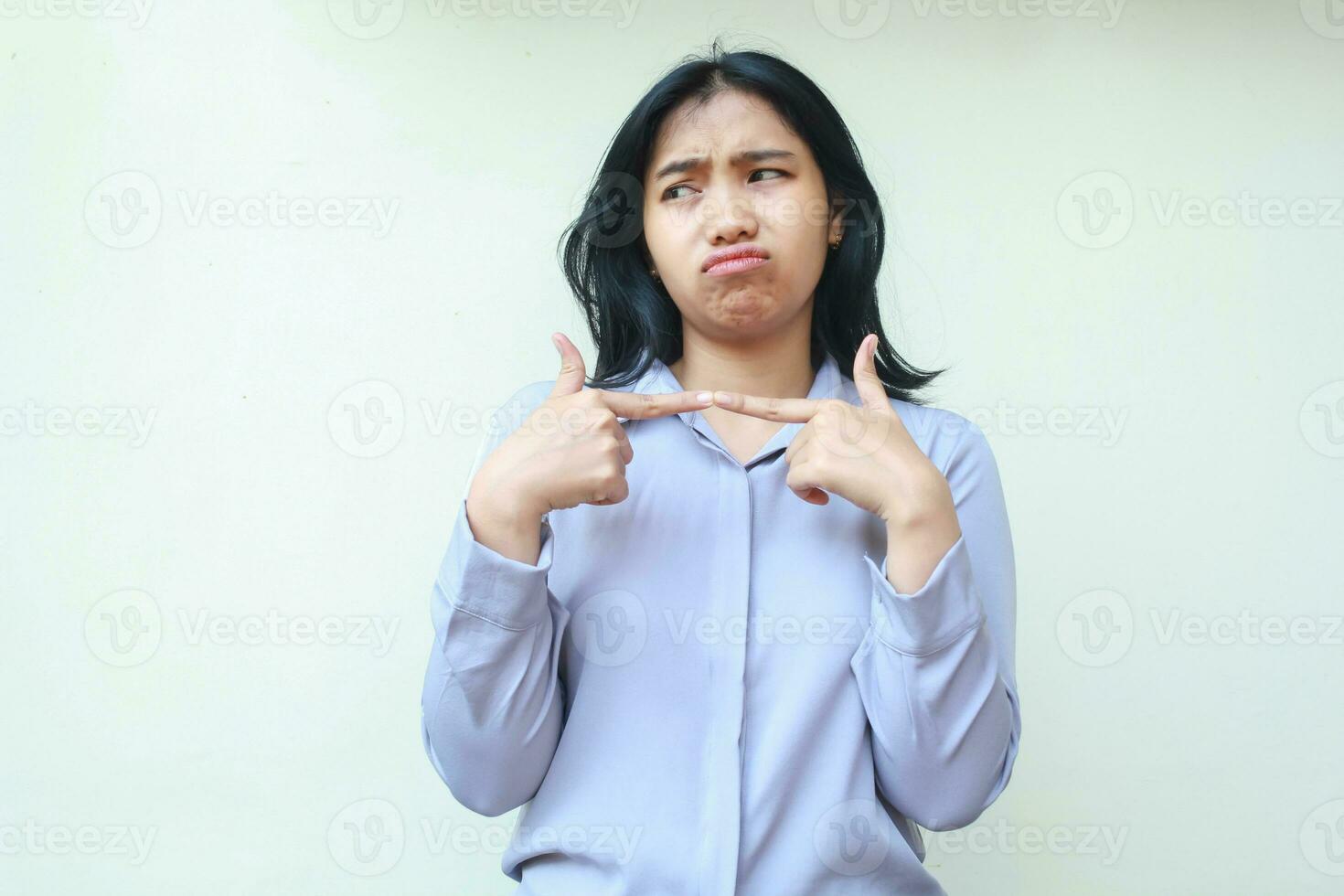 image of sad office girl, sulking asian woman dark haired entrepreneur looking away with stick finger feeling displeased offended wear formal purple shirt standing over isolated white background photo