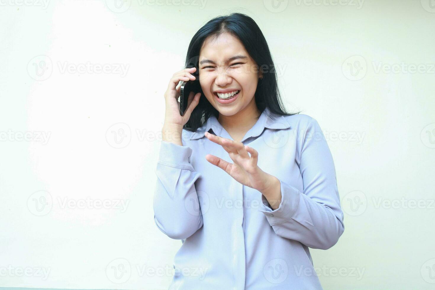 image of delightful asian young business woman laughing happily while speaking on mobile phone, rejoicing winning acvhievement expression, wear purple formal shirt standing over white background photo