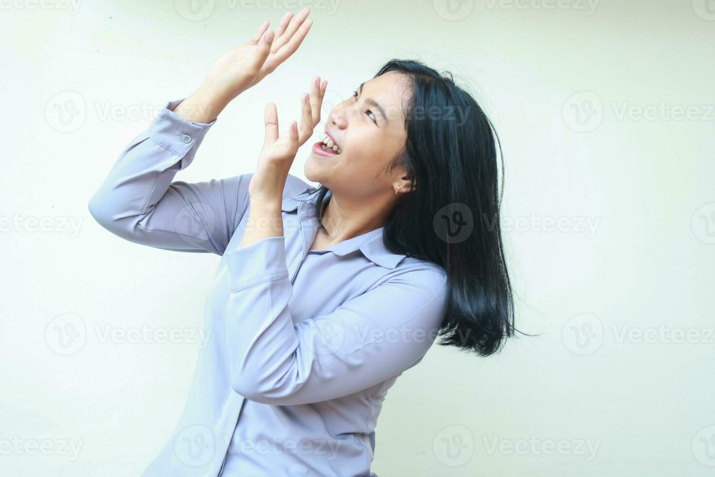 shocked beautiful asian young business woman looking up stunned raising arm try to cover body from falling imaginary product, wearing formal shirt standing over isolated white background photo
