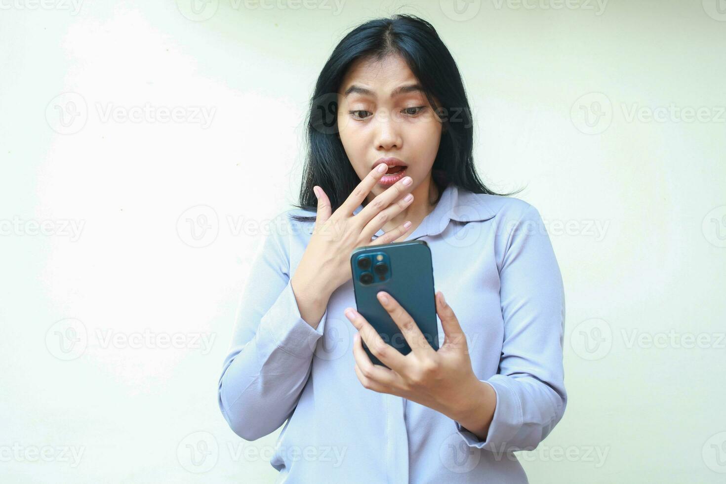 shocked asian young business woman stunned and covering her mouth while looking mobile phone wearing formal shirt standing over isolated white background photo