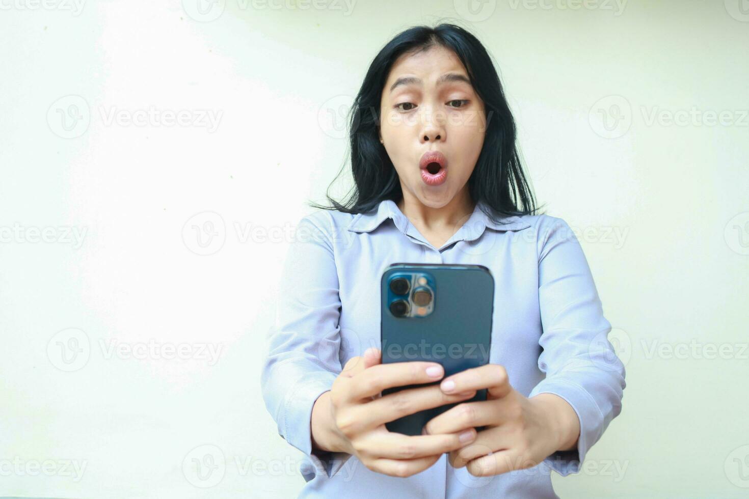 amazed asian young business woman using smartphone shocked with wow expression wearing formal shirt standing over isolated white background photo