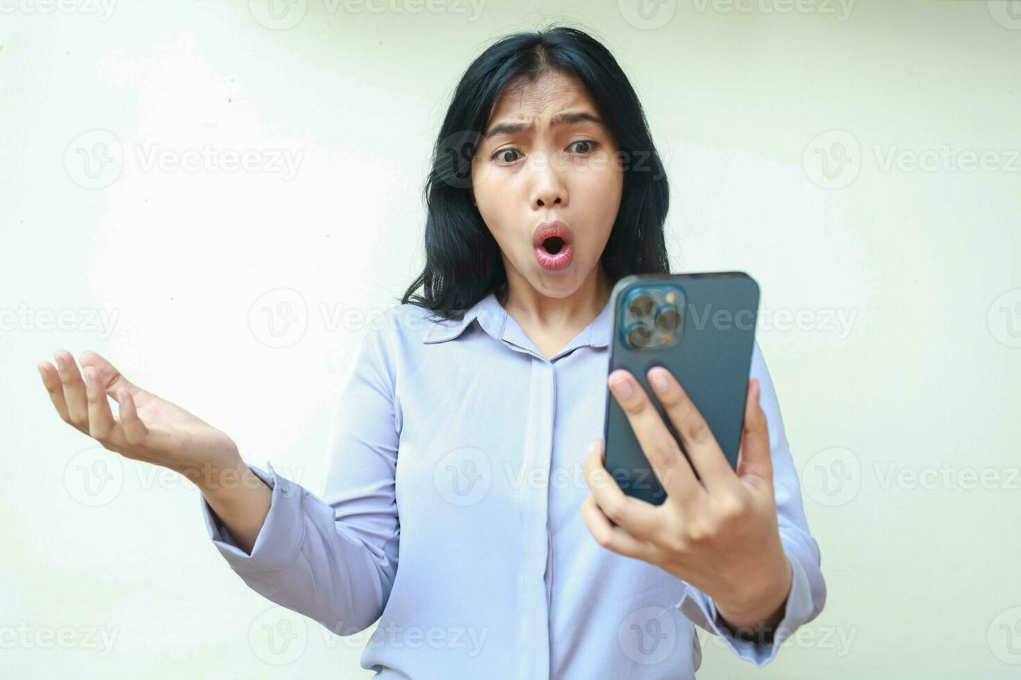 pretty asian young business woman shocked looking mobile phone hold on hands raising palm, questioning gesture, wearing formal shirt standing over isolated white background photo