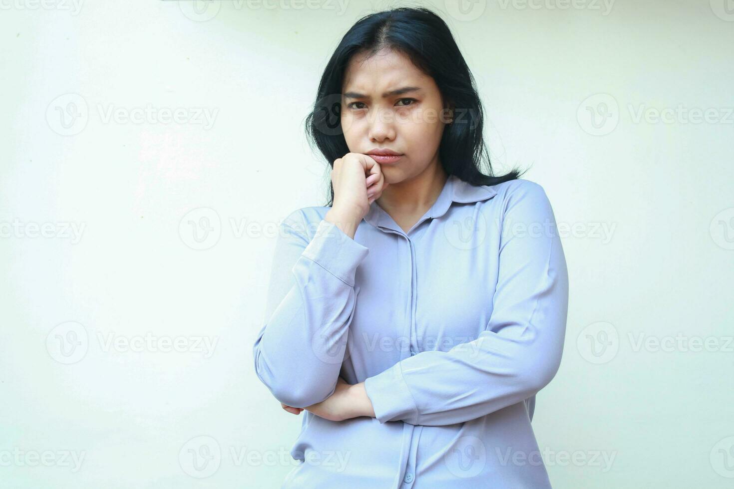 confused asian young business woman folded arm looking at camera with hands on chin show puzzled expression wearing formal short standing over isolated white background photo