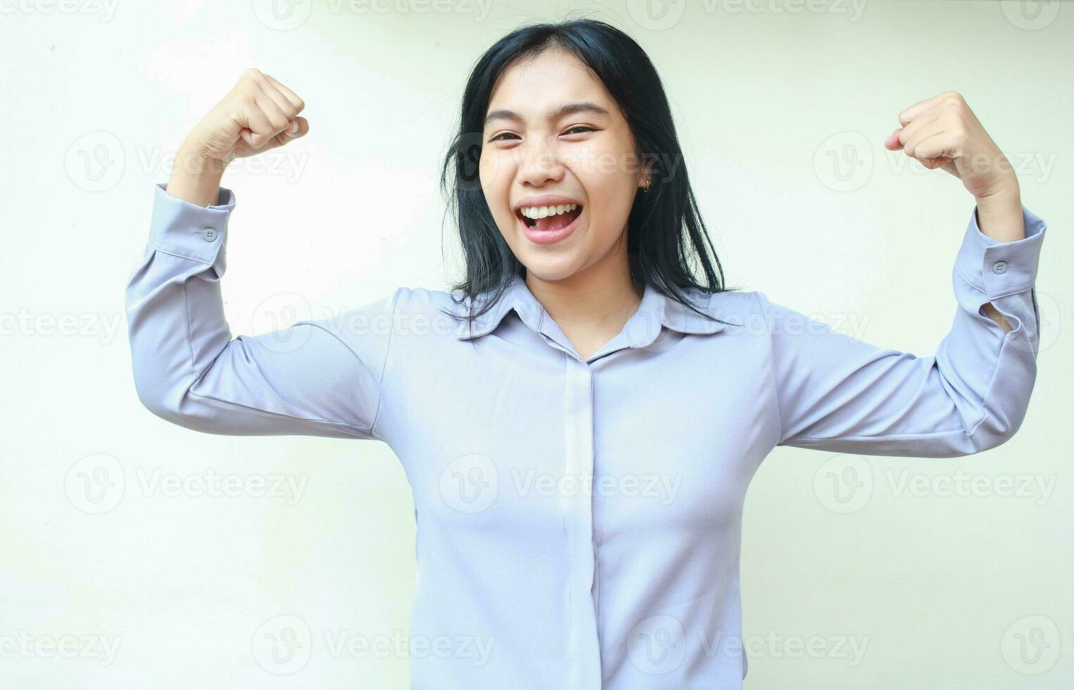 carefree powerful asian young business woman laughing at camera with raising arms showing muscle strength, proud of self achievement, wearing formal shirt standing over white background photo