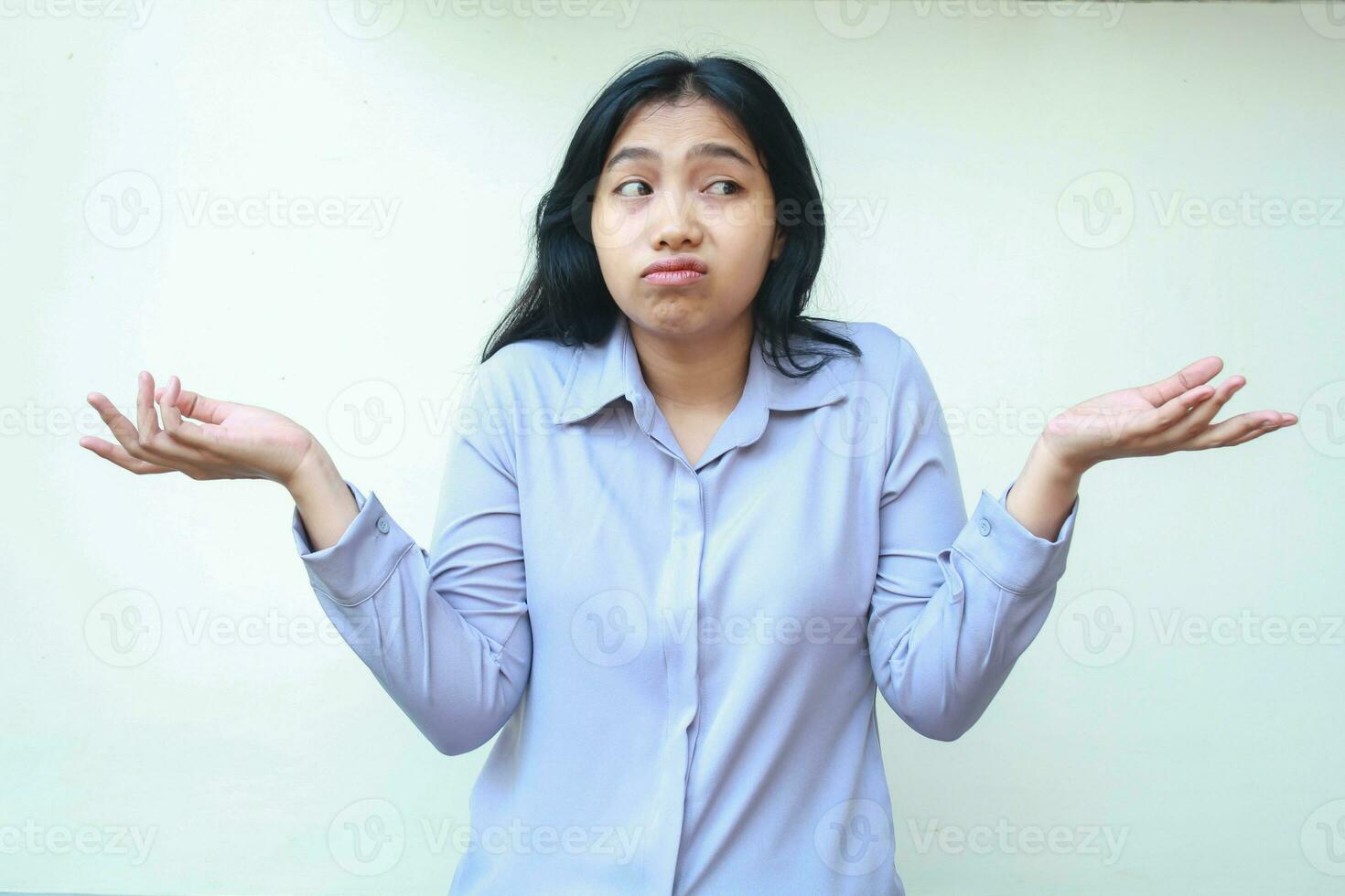 have no idea or maybe gesture. clueless asian young business woman spreads palms sideways confused wearing formal shirt looking away standing over isolated white background photo
