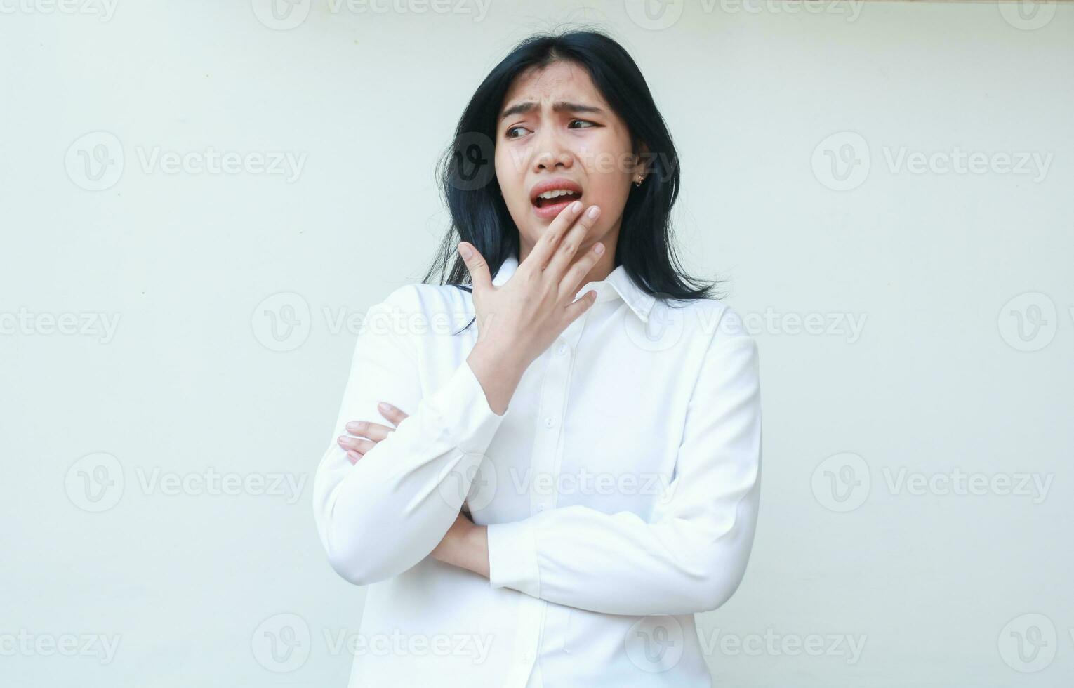 image of shocked asian woman manager wearing white suit shirt looking away stunned unsure with hands on chin arms folded, standing anxious making mistakes, amazed expression photo