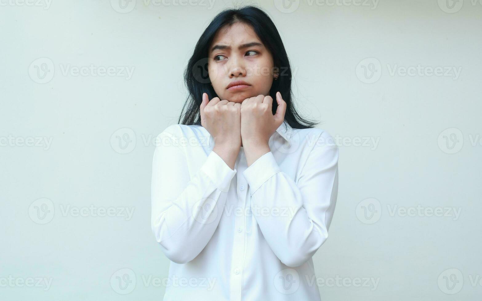studio shot of sad dissappointed asian young business woman executive looking aside pondering with raising fist pump on chin dressed in white formal suit, standing, gloomy face expression photo