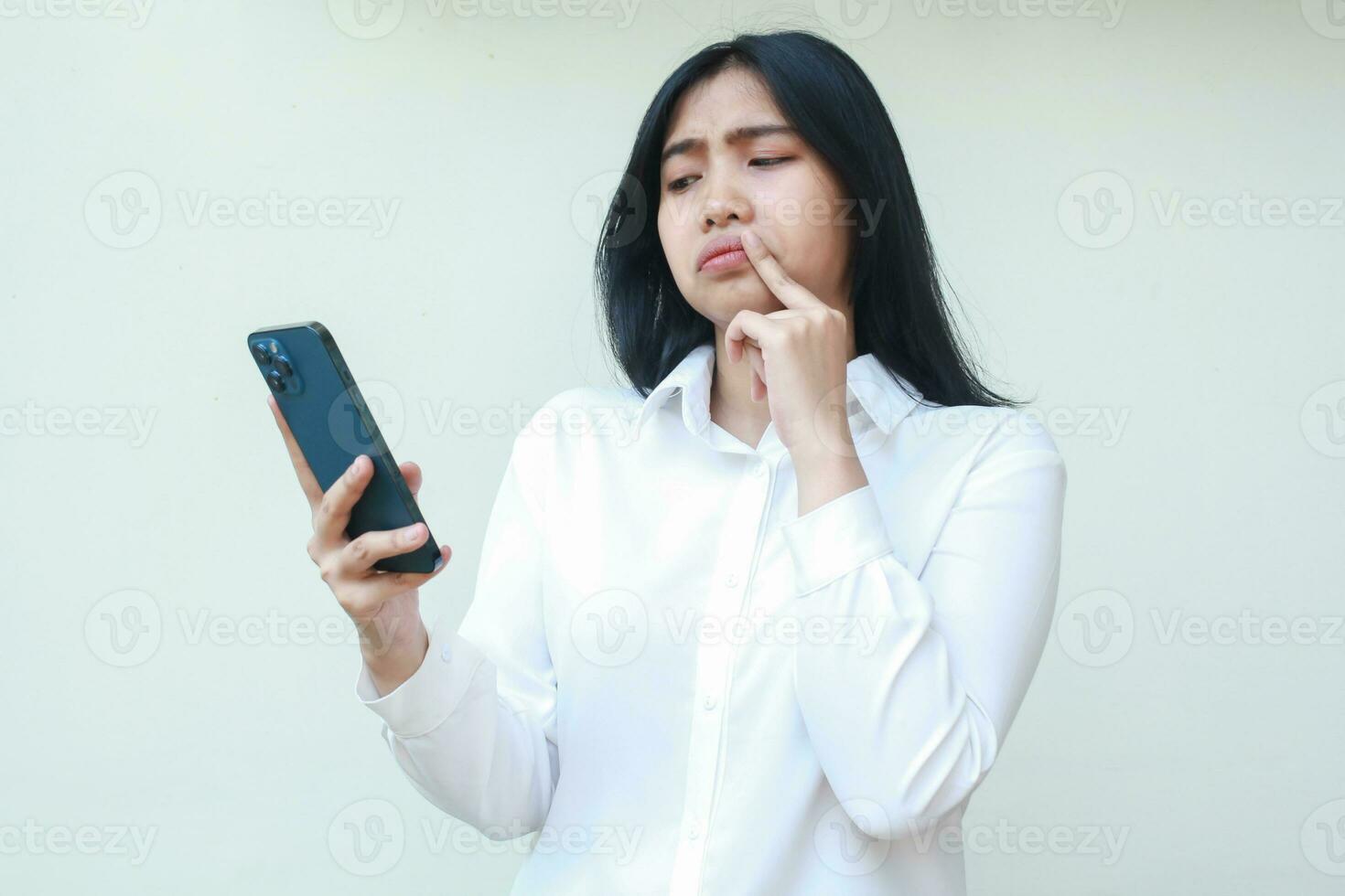 confused asian woman wondering using mobile phone app and social media read news with fist on chin show disbelief facial expression wearing white formal suit standing over isolated background photo