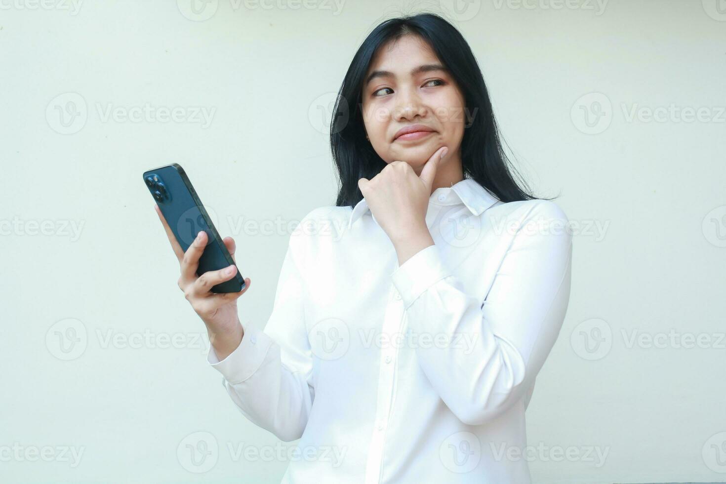 thoughtful asian woman secretary holding mobile phone thinking plan idea, online shopping, surfing social media, looking aside to empty space with hands on chin wear white formal suit standing photo
