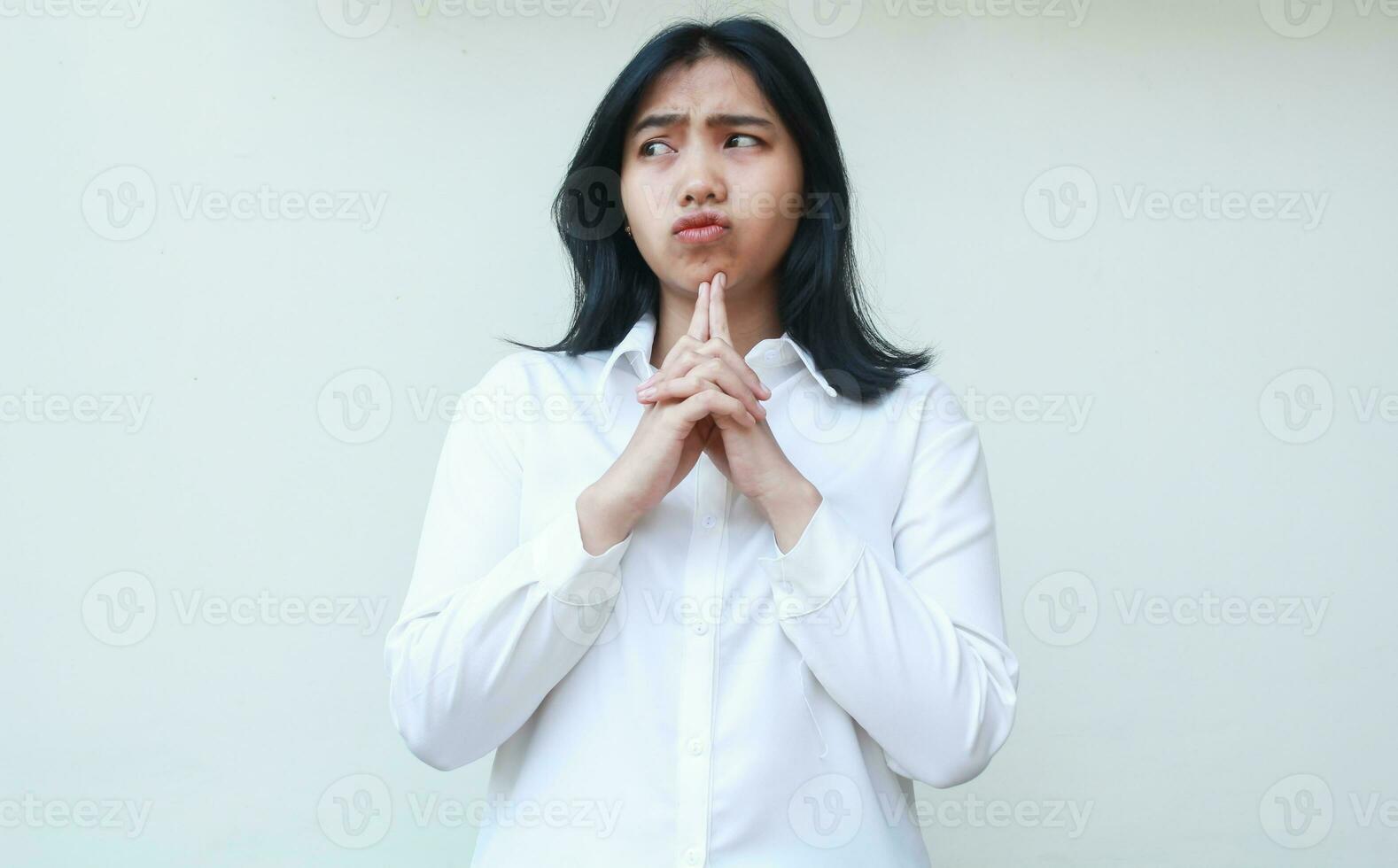 image of pondering asian young woman executive dressed in white formal suit thinking about something looking aside with fingers on chin worrying, daydreaming gesture photo