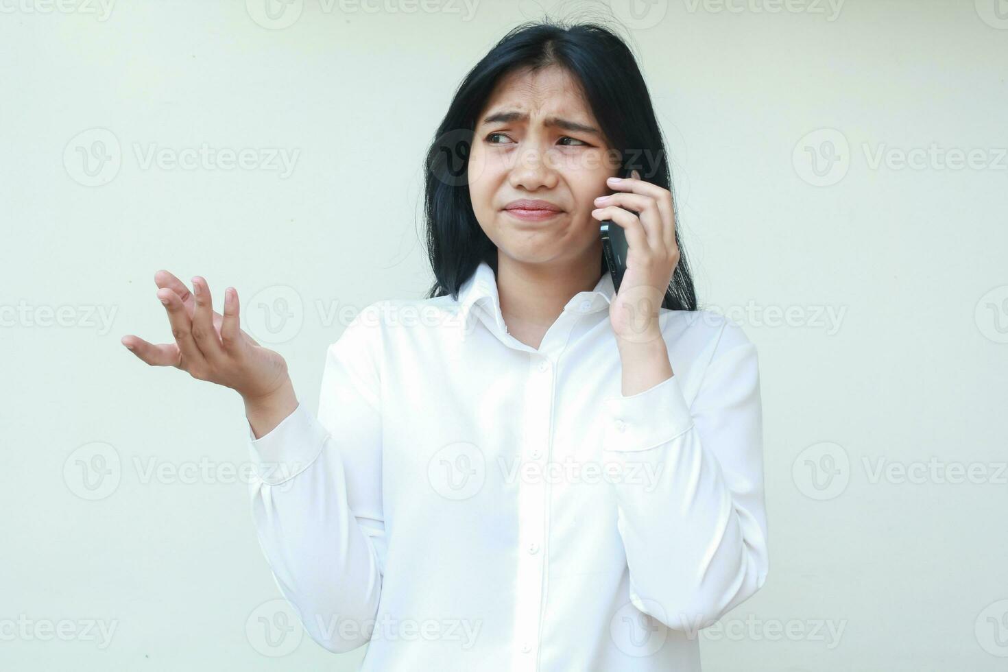 image of clueless asian young business woman raising palms worried speaking on smartphone wear white formal shirt, have no idea gesture questioning solution, frustrated expression, standing photo