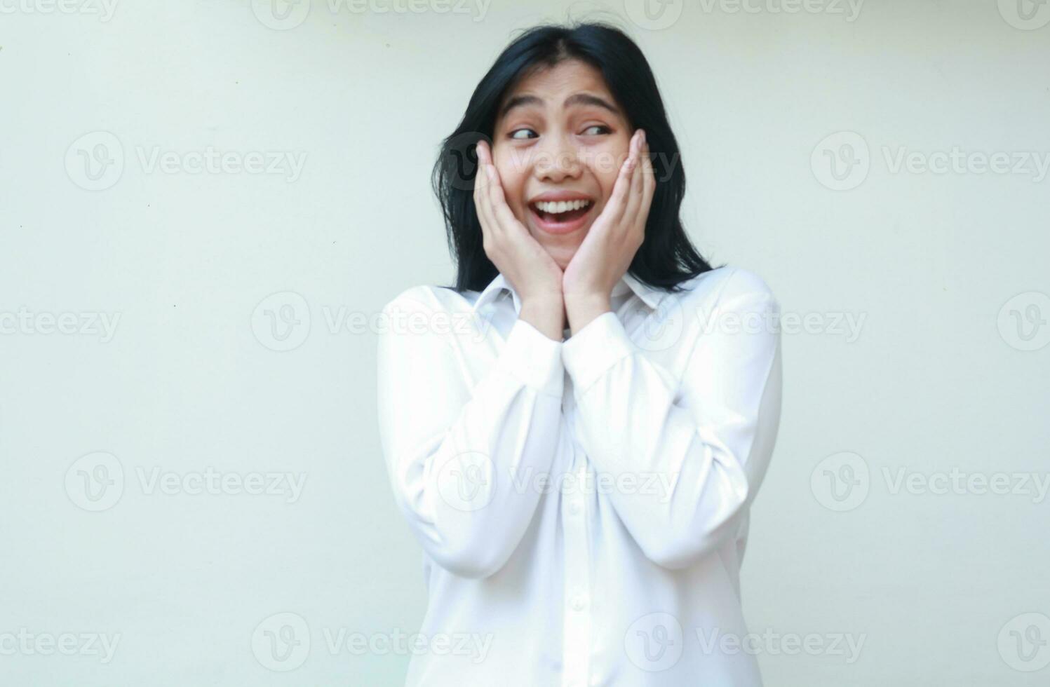 carefree asian young business woman shocked looking aside at empty space wearing white formal suit shirt, touching her face with two palms surprised, standing over isolated background photo