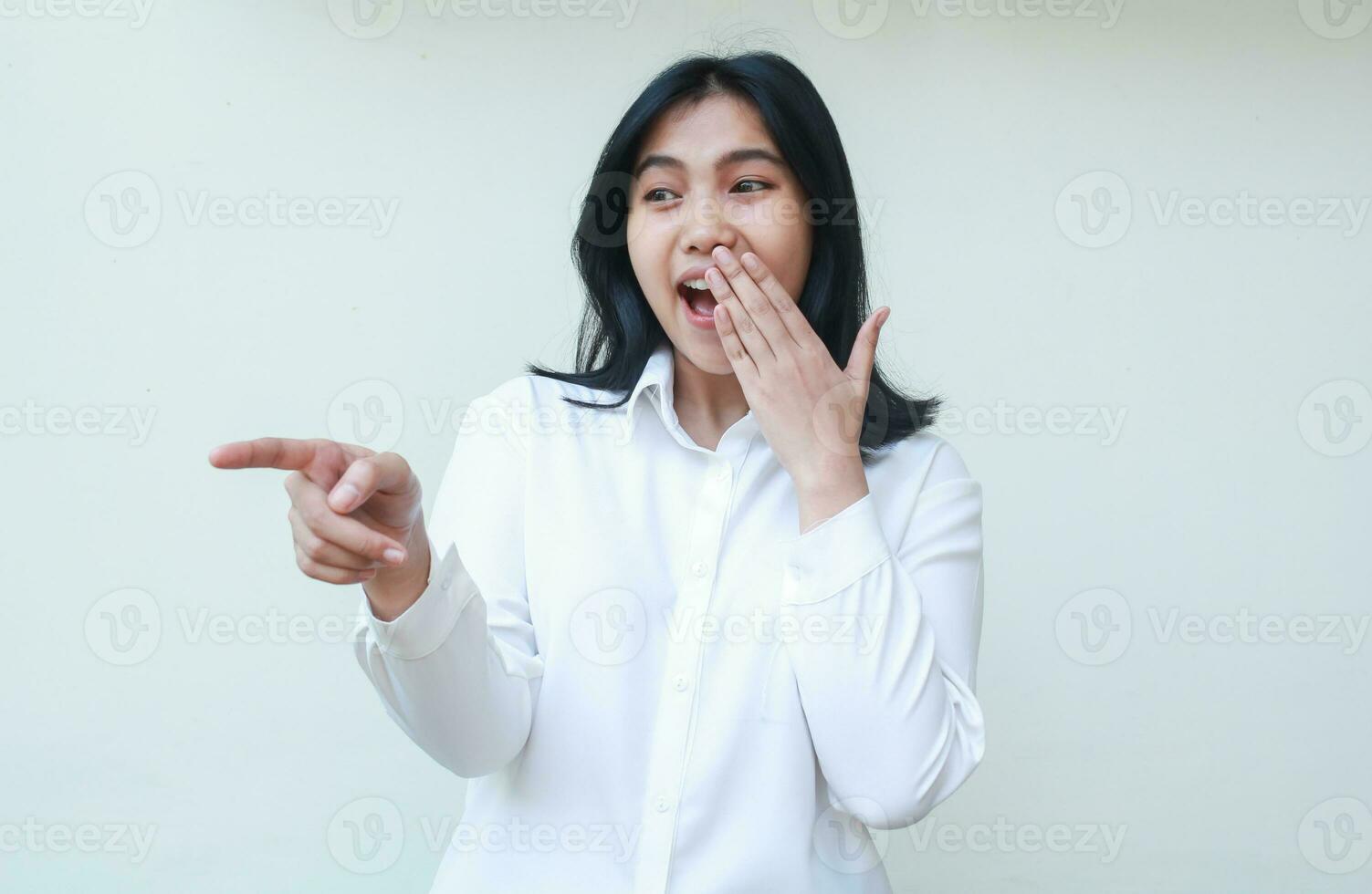 carefree surprised asian young business woman pointing forefinger amazed covering her mouth wearing white formal suit shirt, feeling shy embarrassed and shame, isolated on white background photo