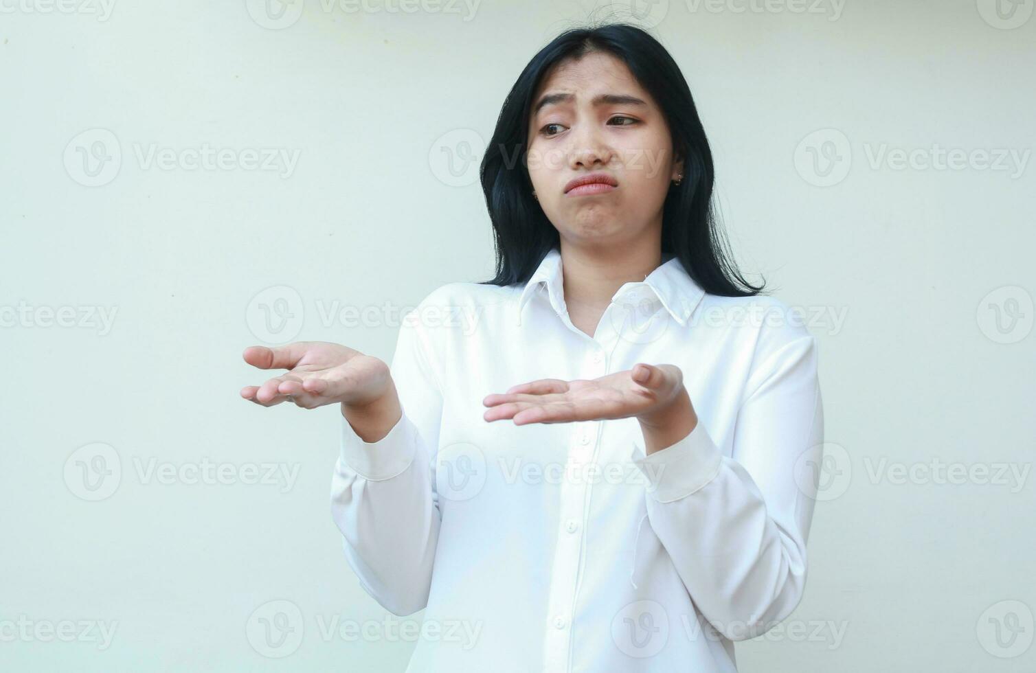 portrait of pondering asian young business woman executive wearing white formal shirt looking away daydream with shrugging shoulders raising open palms, showing and presenting gesture photo