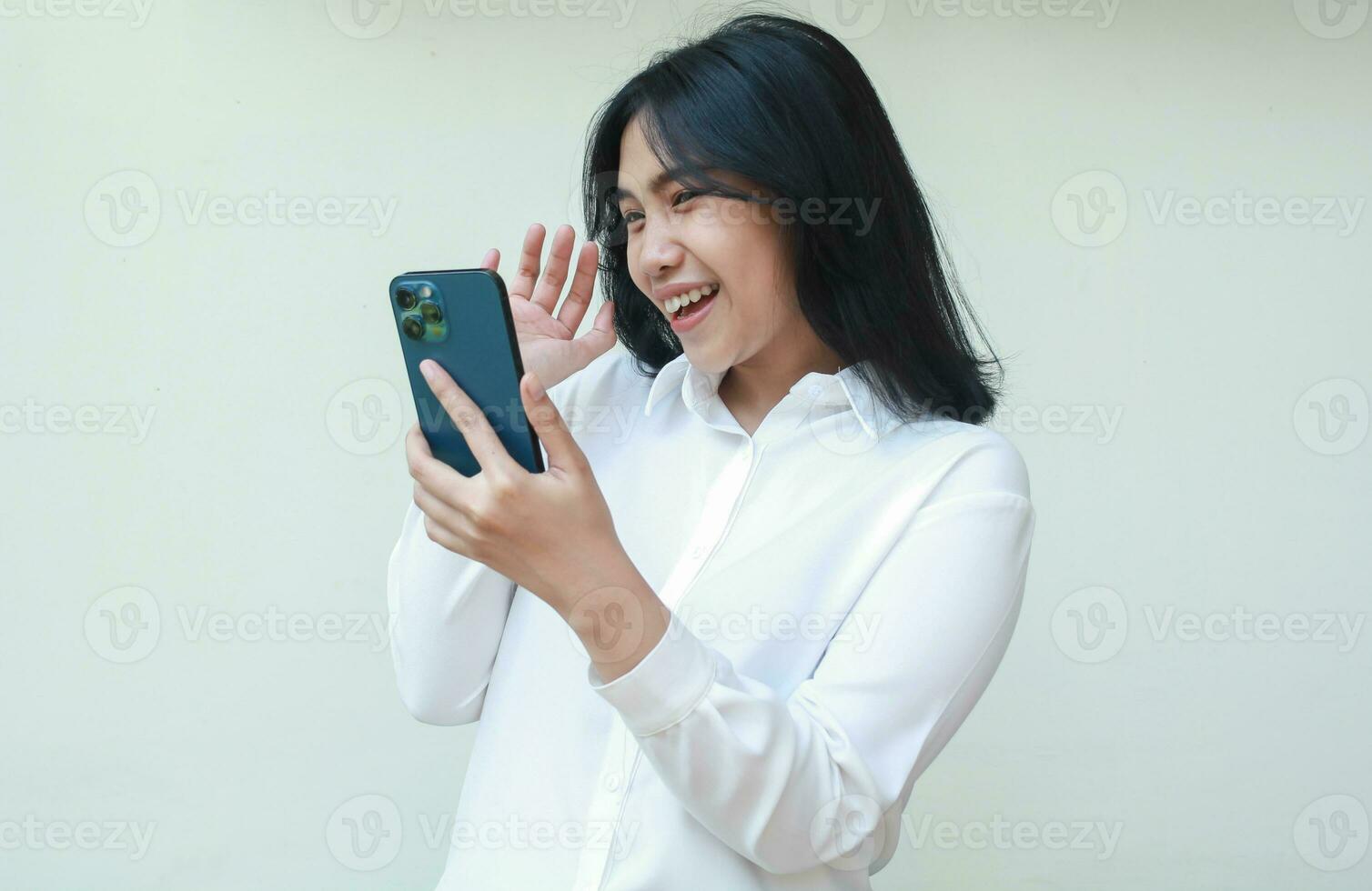 image of success excited young asian saleswoman holding smartphone waving palms say hi welcoming gesture wearing white suit shirt, playful female said hello in social media, video call, standing photo