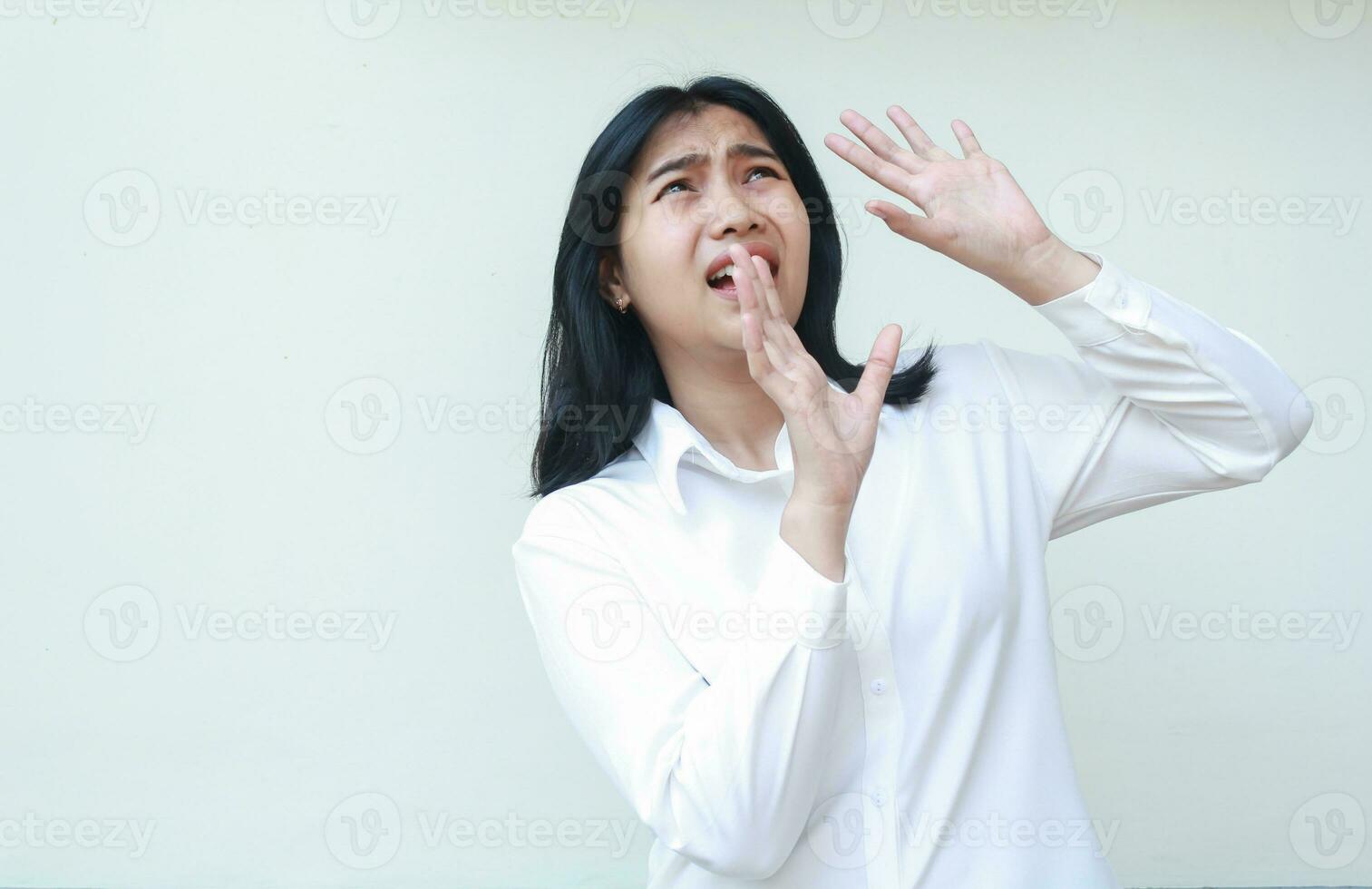 portrait of terrified asian business woman raising palms and looking up with scared face expression wearing white shirt formal suit standing over isolated background photo