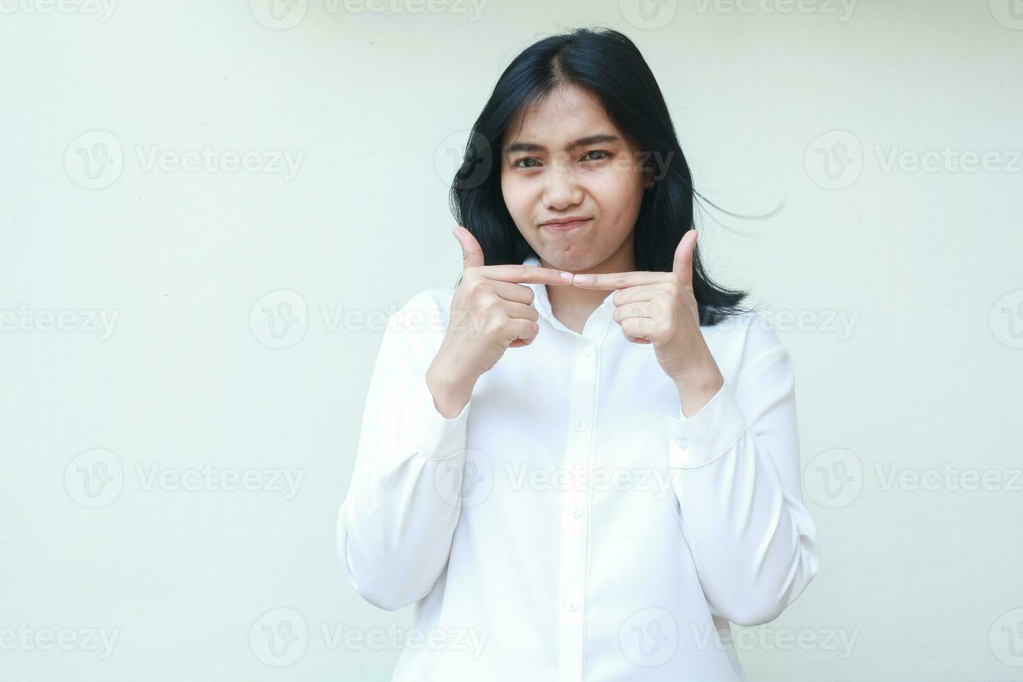 studio shot of gloomy cute asian business woman stick finger together wearing white shirt formal suit looking at camera show demanding expression standing isolated photo