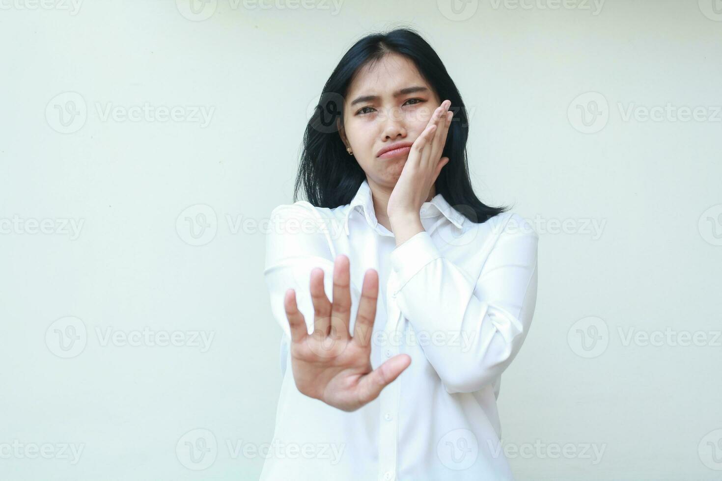 portrait of sad tired asian business woman wearing white shirt formal suit reaching hands towards camera showing stop signs and leaning face on palms standing isolated background photo