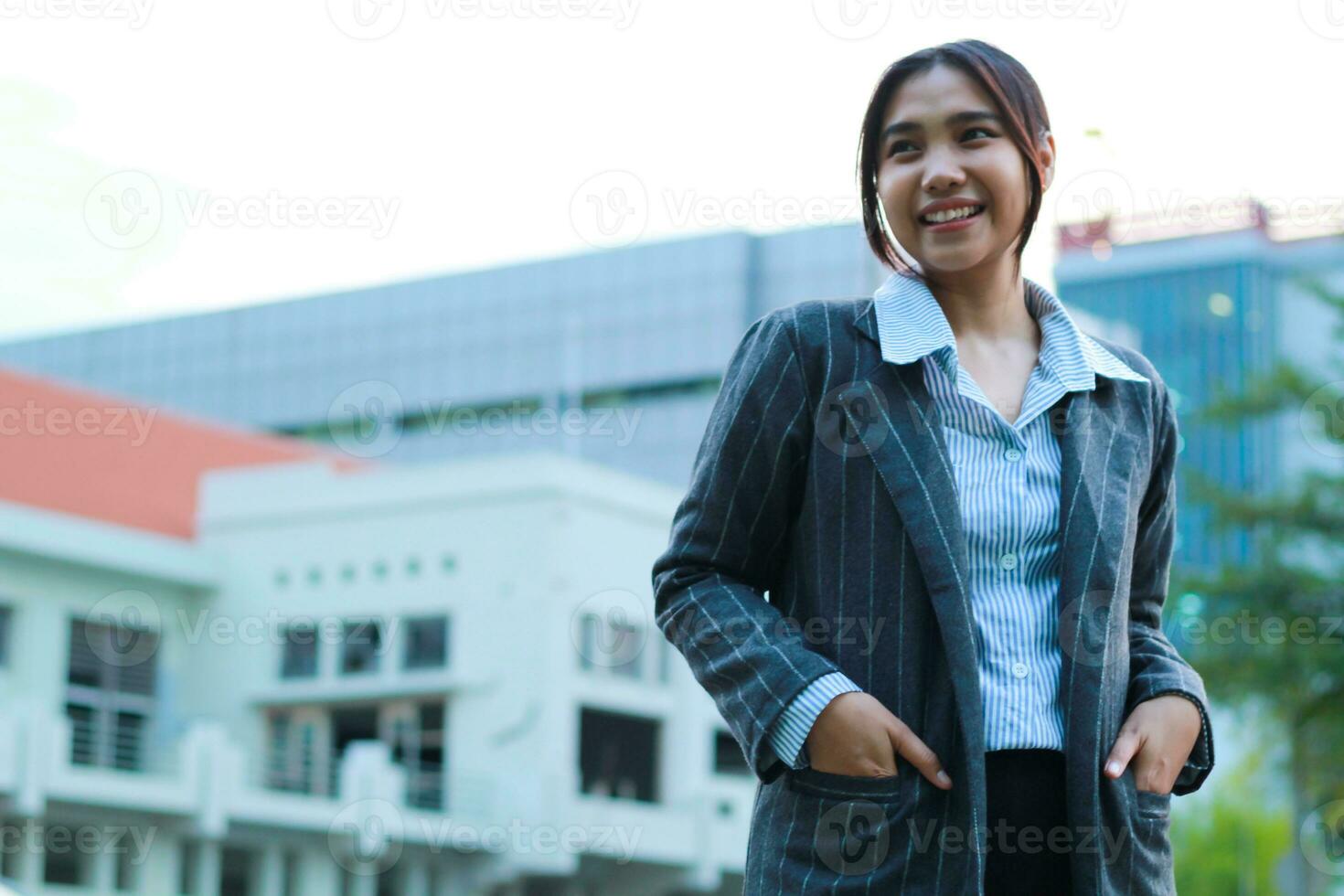 imagen de exitoso asiático negocio mujer caminando en ciudad calles con urbano edificio antecedentes mirando lejos confidente vistiendo formal traje, hembra inversión gerente en pie en al aire libre sonriente foto