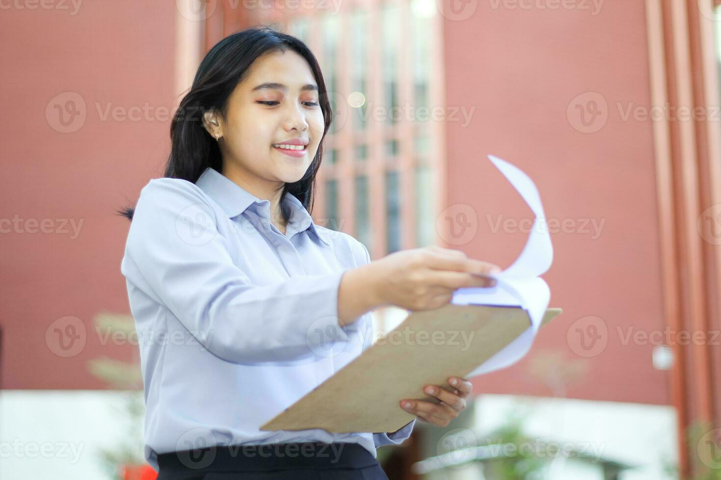 confident relax asian financial adviser reading paper document wearing formal suit standing in outdoors, smiling business woman accountant review tax report while walking over office building photo