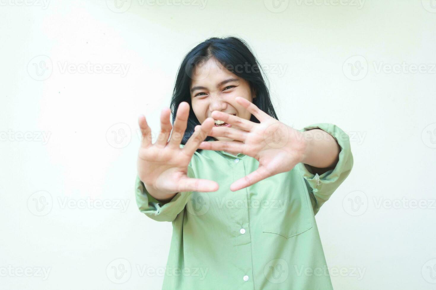 despreocupado asiático mujer levantamiento palmas adelante demostración detener gesto vistiendo verde de gran tamaño camisa mirando a cámara con riendo emoción cara expresión aislado en blanco antecedentes foto