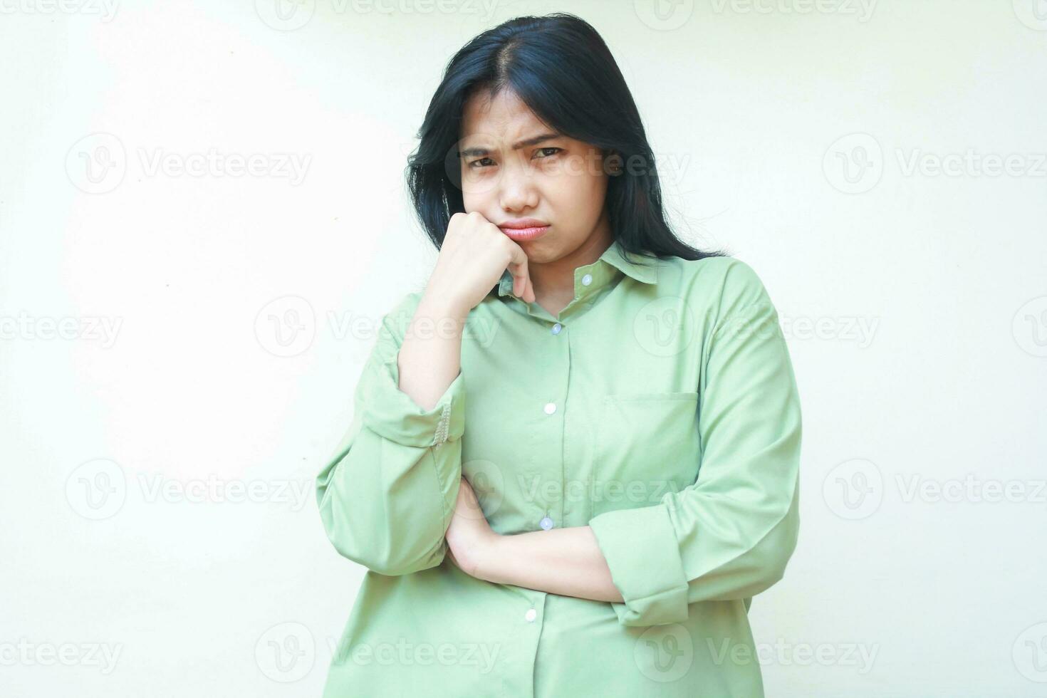 depressed asian woman with dark hair looking at camera with sad gloomy face expression folding arms and hands on chin wearing green oversized shirt isolated on white background photo