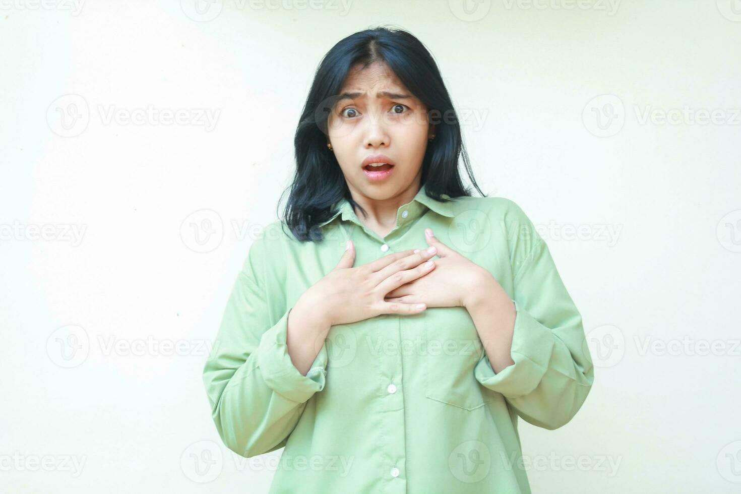 conmocionado oscuro pelo asiático mujer vistiendo verde de gran tamaño camisa conmovedor cofre y mirando a cámara aturdido y sensación culpable, demostración incredulidad expresión aislado en blanco antecedentes foto