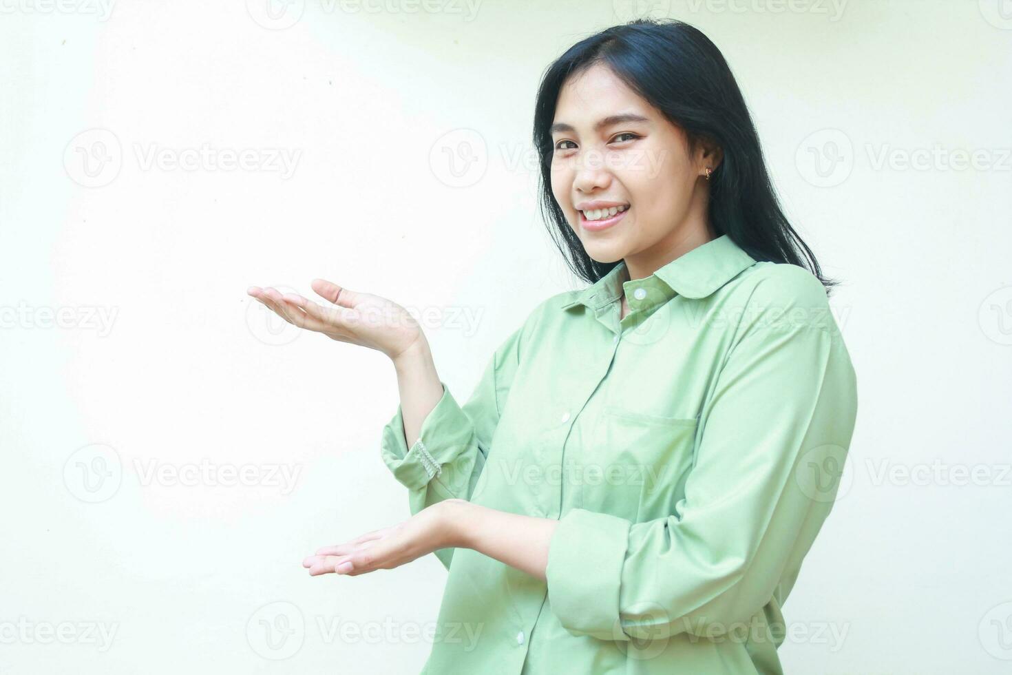 content amused pleased asian woman with dark hair raising palms to side of empty space showing presenting gesture new product wearing green over size gesture standing isolated white background photo