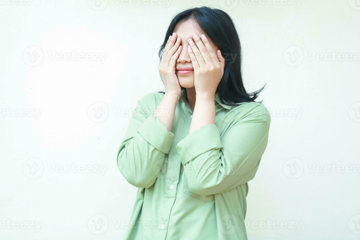 hermosa oscuro pelo asiático mujer vistiendo verde terminado Talla camisa cubierta cara con manos palmas esperando para sorpresa en pie aislado blanco antecedentes foto