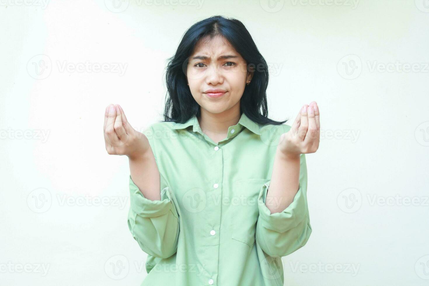clueless asian woman with dark hair looking at camera with confusion expression raising two palms sideways with curled up finger wearing green oversized shirt, showing and presenting gesture photo