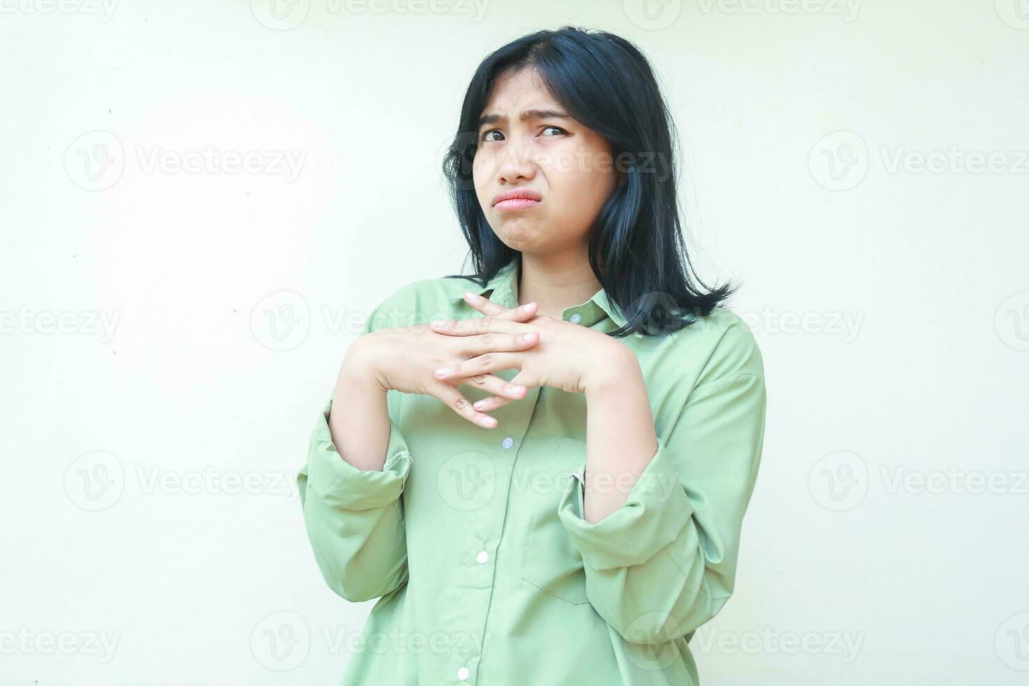 thoughtful asian woman with dark dark hair wearing green oversized shirt looking away with stick finger thingking about something isolated on white background photo