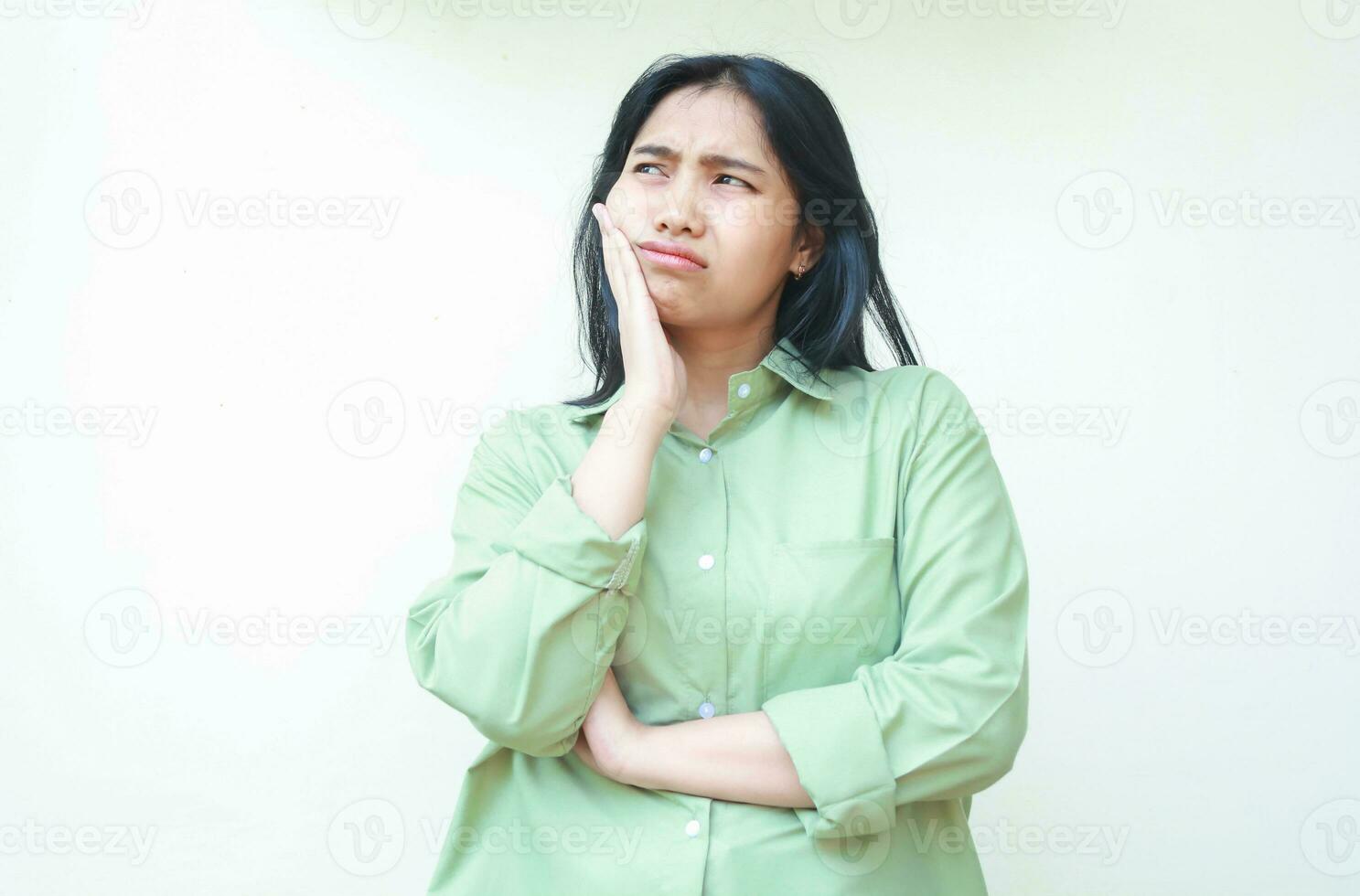 Deprimido asiático mujer con oscuro pelo mirando lejos espectáculo triste melancólico cara expresión con plegable brazos y manos en barbilla vistiendo verde de gran tamaño camisa aislado en blanco antecedentes foto