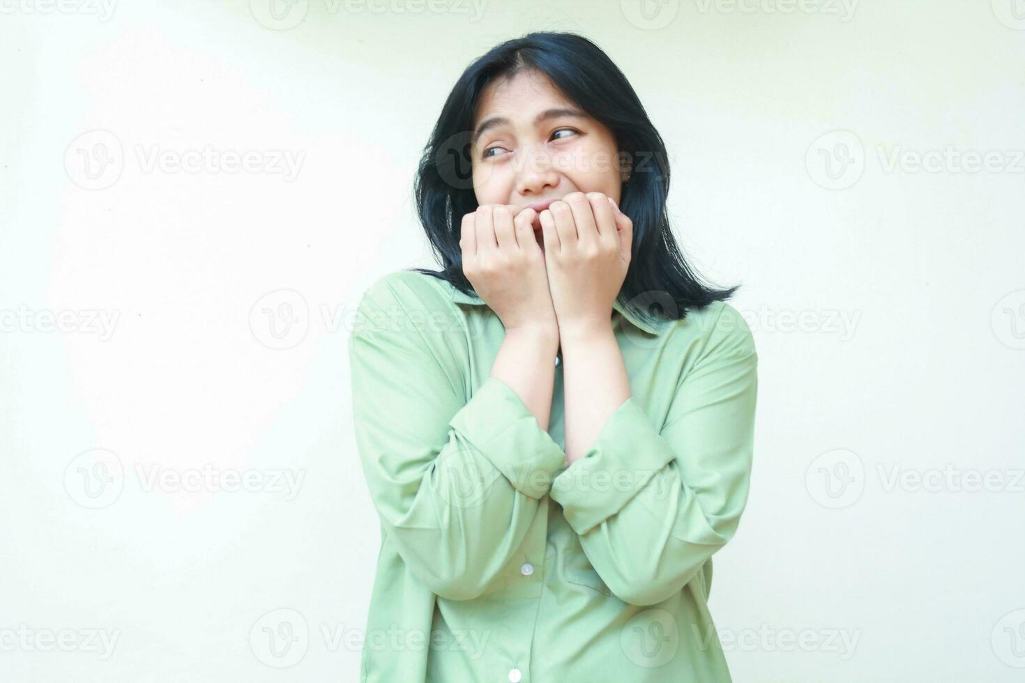 infeliz asustado asiático mujer vistiendo verde demasiado grande camisa mordedura su uñas sensación temeroso y asustado mirando aparte a vacío espacio pensando alguna cosa en pie aislado en blanco antecedentes foto