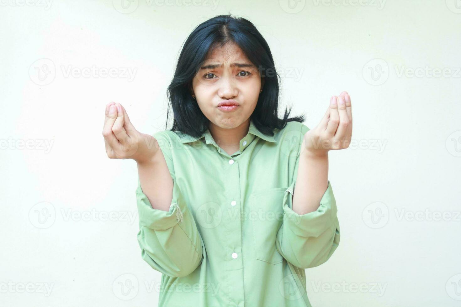 clueless asian woman with dark hair looking at camera with confusion expression raising two palms sideways with curled up finger wearing green oversized shirt, showing and presenting gesture photo