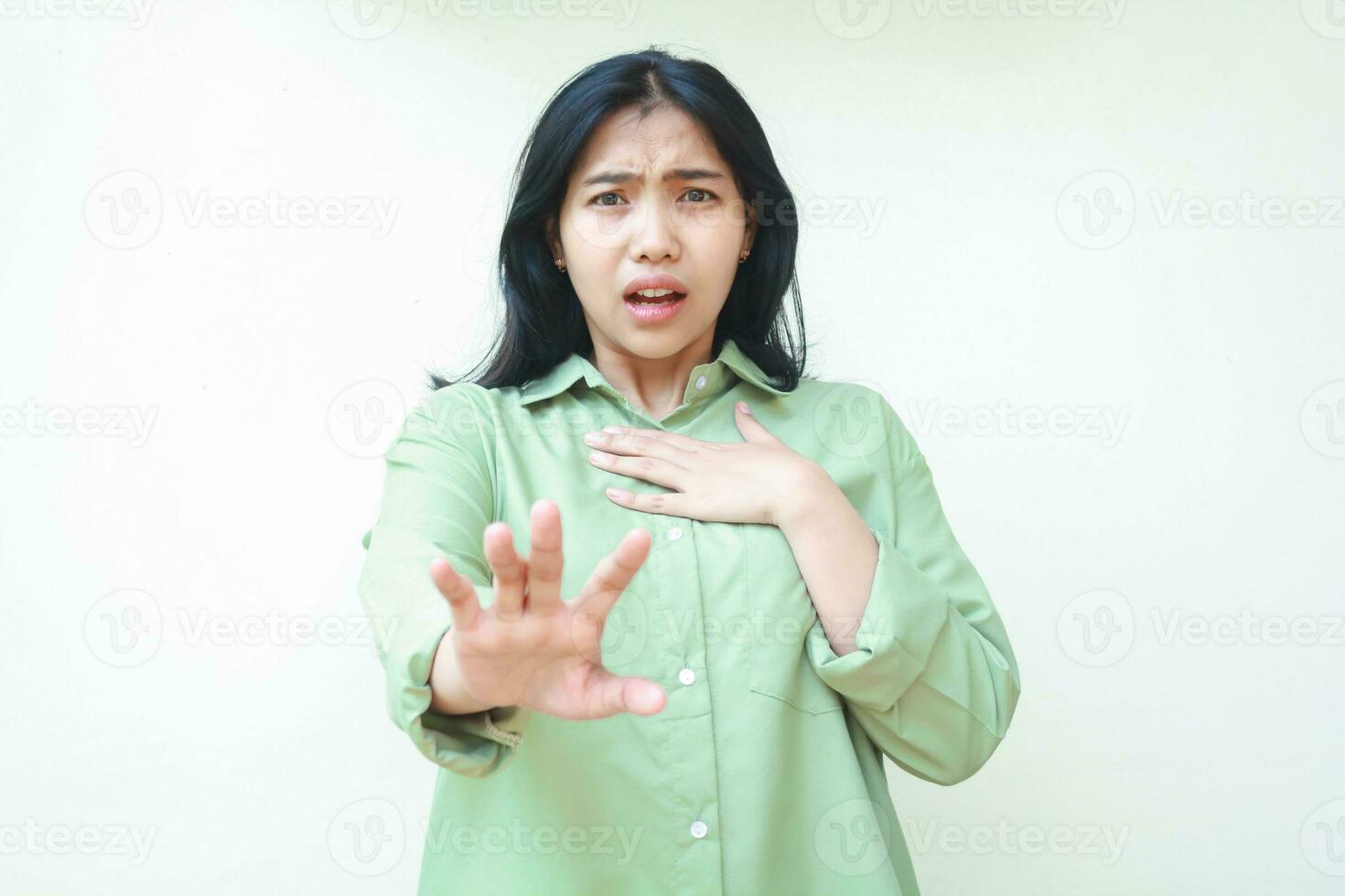 shocked dark hair asian woman reaching hands forward and touching her chest with palms stunned showing disbelief expression wearing green oversize shirt isolated on white background photo
