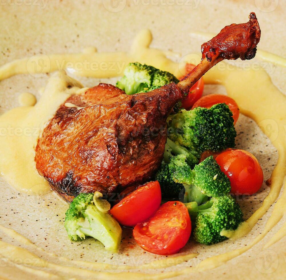 Confit duck leg with broccoli and tomatoes photo