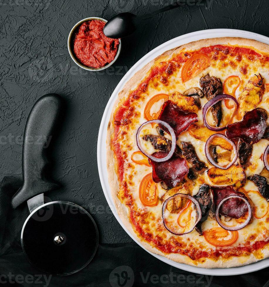 pizza on cutting board with cutter nearby, top view photo