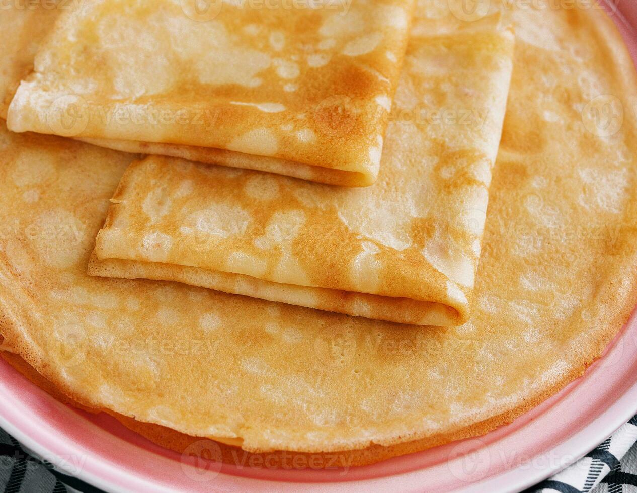 Stack of fresh thin pancakes on pink plate photo