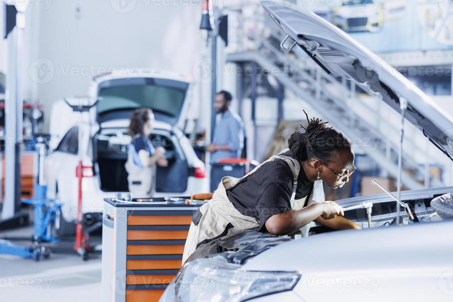 Mechanic in car service picking torque wrench from work station bench, using it to tighten bolts after replacing engine. African american garage worker uses professional tools to fix client automobile photo