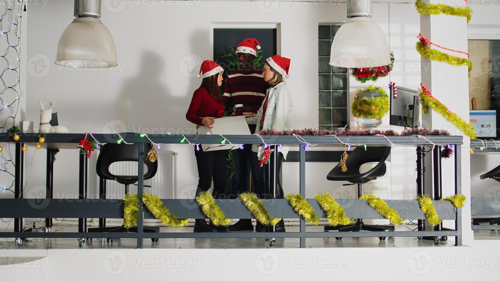 Upset asian worker in xmas ornate office packing desk belongings on last day at work after being fired. Sad employee getting consoled by colleagues after being laid off before Christmas photo