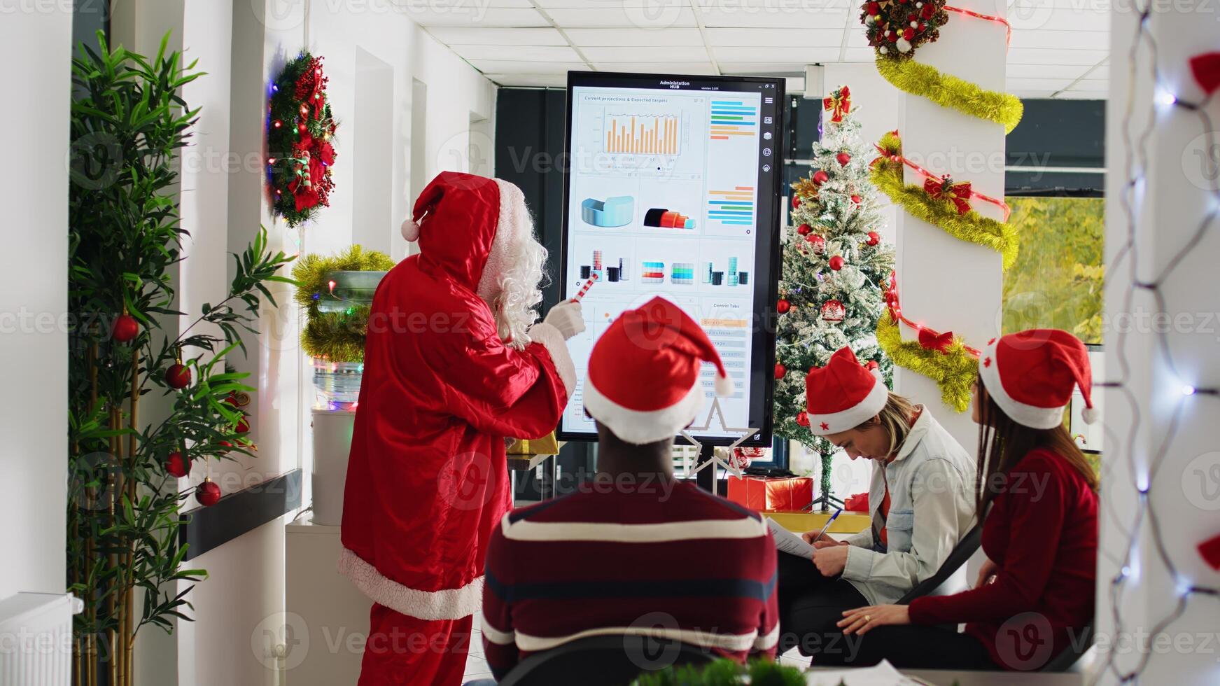 Experienced speaker dressed as Santa Claus doing presentation in front of company workers using candy cane pointer. Employees learning how to advance their career during Christmas business meeting photo