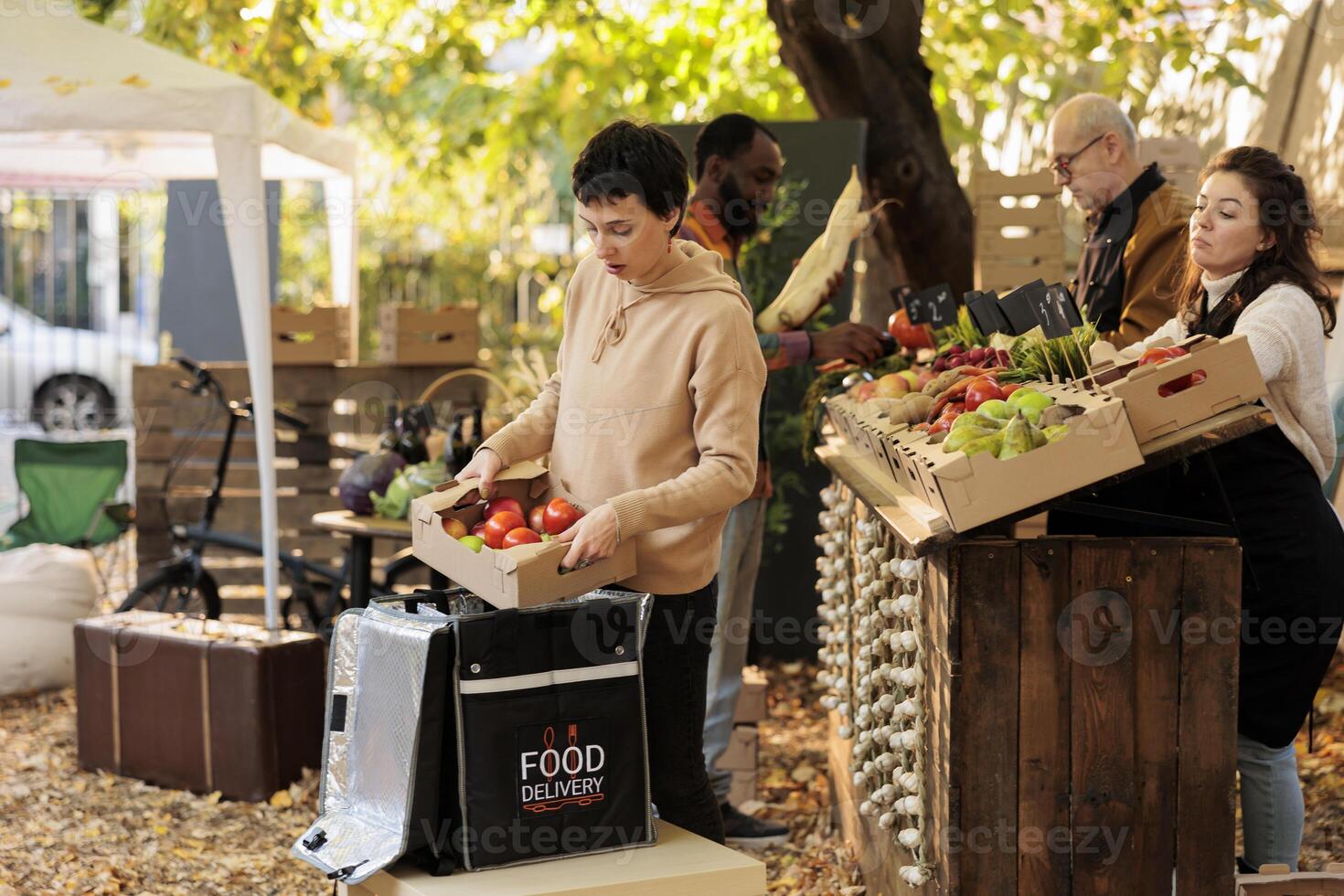 Food delivery worker putting fresh natural produce box in bag and standing at local food market. Farmers delivering healthy bio fruits and vegetables to customers from farm to doorstep on bike. photo