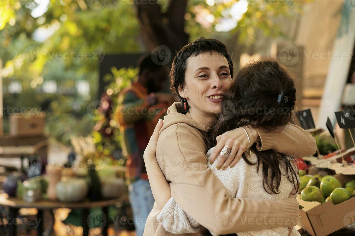 Friendly farm stand seller hugging happy loyal client before selling organic fruits and vegetables. Local grocery store owner greeting regular customer, being cheerful at food marketplace. photo